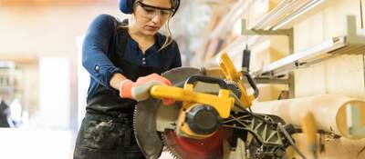 A female carpenter using a circular saw in a woodshop.