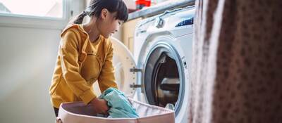Little girl unloading the washing machine while helping her mom with laundry at home