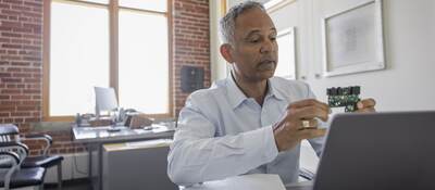 Male engineer at laptop explaining semiconductor on video call in meeting.