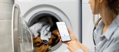 Woman controls washing machine with a smartphone.