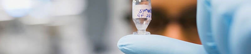 Gloved hand holding a chemical vial in a laboratory setting