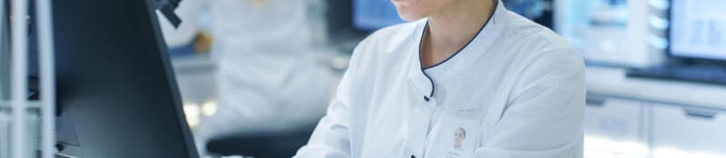 A scientist in a lab setting typing on a computer. 