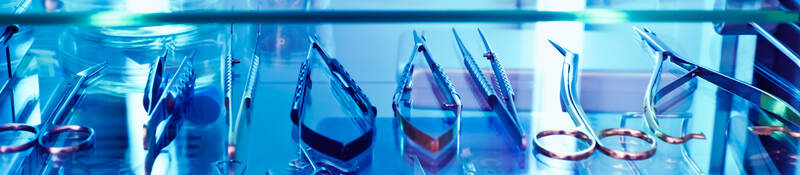 Medical tools sit on a shelf under the blue glow of ultraviolet light, used as a germicidal disinfectant.