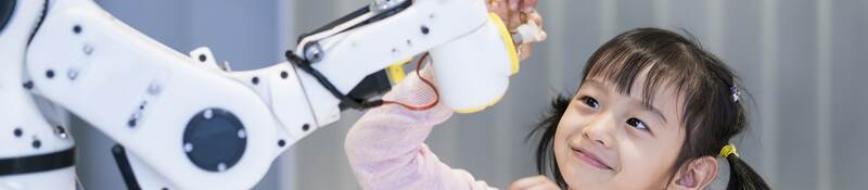 A young girl looking at a robotic arm.