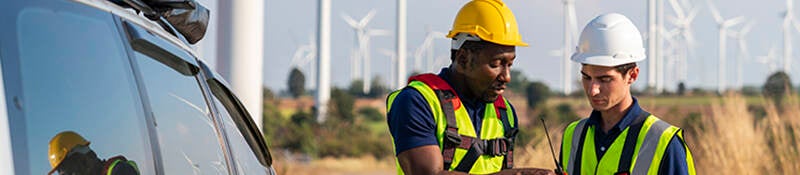 Two engineers having a discussion in front of a wind farm