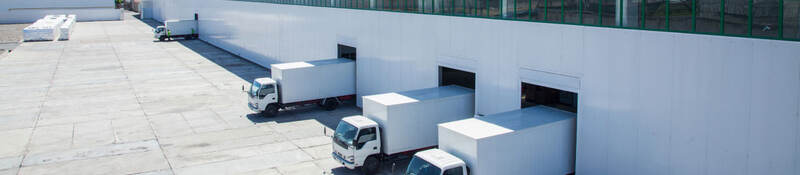 3 white trucks docking at a modern white building