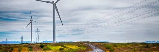 A wind turbine set to the left of a rural expressway.