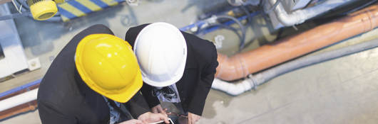 Two men in hard hats on a factory floor consulting over a tablet.