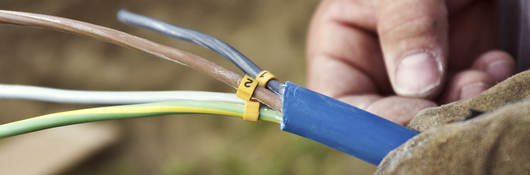 A close-up of a man’s hand holding a cable with exposed wiring. 