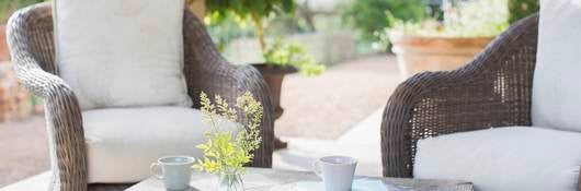 An vignette of two brown wicker chairs solidly resting on an outdoor patio.