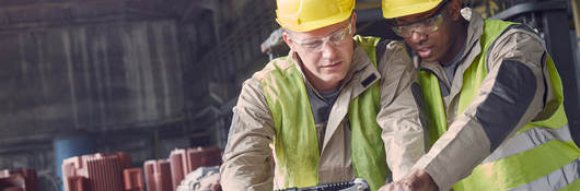 two men in protective gear look at a laptop