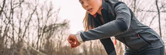 A female runner checks her time on her smart watch. She's wearing black on black performance material workout gear.