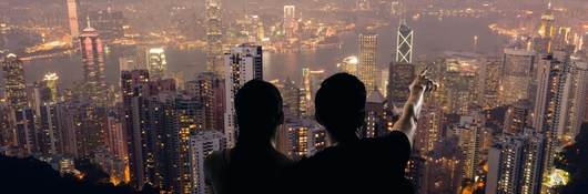 Silhouette of couple sit on ground point faraway on the roof above the city in the night.