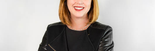 Jen Scanlon, CEO of UL, poses in front of a grey background wearing a black jacket and black dress