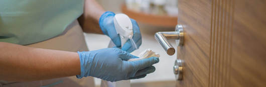 Employee spraying disinfectant on cloth to sanitize door handle