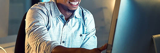 Smiling man sitting at a desk in front of a computer monitor