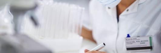 Female medical professional wearing protective eyewear and facemask making notes on electronic device