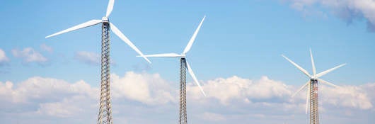 Wind turbines on a treeless hill under a blue sky with billowy clouds