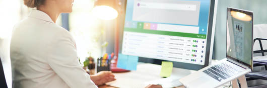 Woman sitting at desk in front of a computer monitor and laptop computer