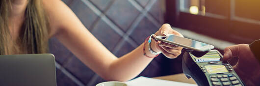 woman tapping a mobile phone for payment in cafe