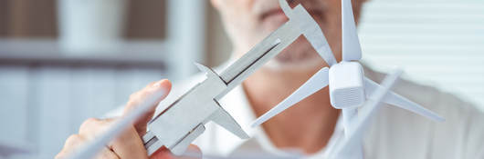 Person measuring a scale model of a wind turbine with calipers