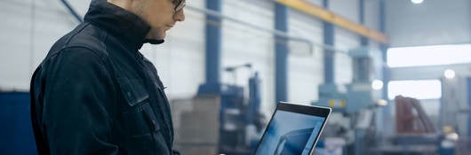 Factory worker in a hard hat is using a laptop computer with engineering software