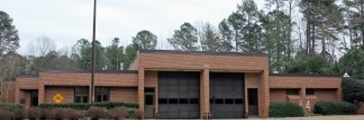 Brown brick firehouse in Cary, North Carolina with two garage bays and the U.S. flag