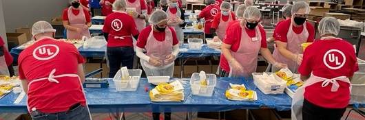 Wide shot of UL employees in red shirts packing meals for Impact 100. 