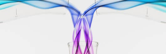 Two beakers pouring colorful liquids into another beaker