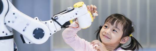 A young girl looking at a robotic arm.