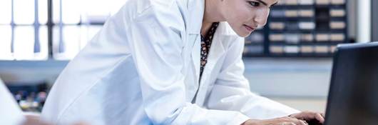 Person in white coat typing on lap top