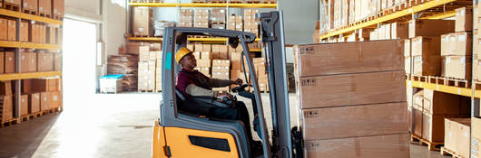 Worker using forklift to move boxes in a warehouse.