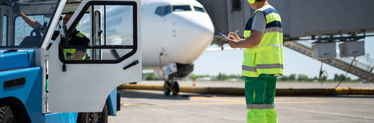 Worker taking notes at airfield while colleague sits in tug cab