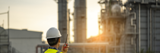 Engineer in hard hat and safety vest talking on radio in front of project site at sunrise. 