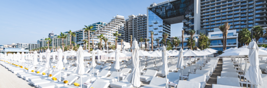 modern beach resort hotel with white chaise lounges and sun umbrellas in the foreground