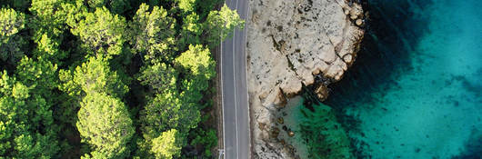 Aerial view of empty road winding between sandy shore and green forest