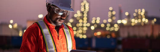Engineer using tablet near an oil refinery at night