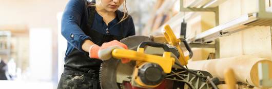 A female carpenter using a circular saw in a woodshop.