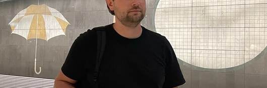 Bart Reuvenkamp stands in front of mural in black t-shirt. 
