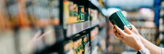 Close up of a woman grocery shopping in supermarket. Holding a tin can and reading the nutrition label at the back.