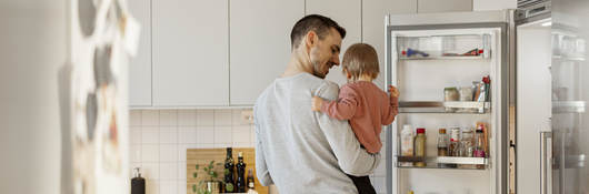Father holding a child and opening a refrigerator door