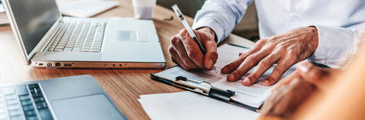 Closeup of a person taking notes on a clipboard while using two laptops