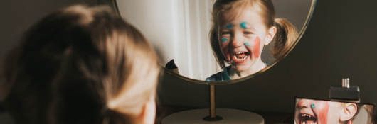 A child playing with makeup and looking in a mirror, laughing