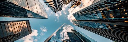 Upward view of the blue sky surrounded by towering skyscrapers