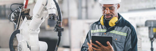 Engineer working on a tablet in front of a mechanical arm in a factory