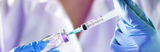 Closeup of a medical professional's hands in blue gloves holding syringe and vial.