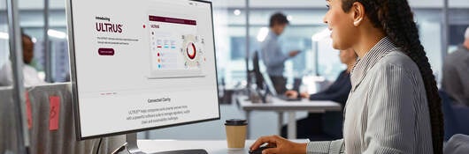 Woman viewing ULTRUS website on computer at her desk sitting in glass-walled office 