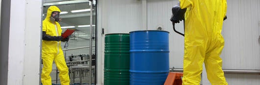 Two people wearing protective clothing and working with a chemical barrel delivery