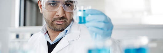 A scientist examining a blue liquid in a beaker