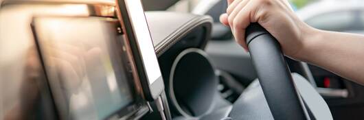 Male driver hand holding on steering wheel using smartphone for GPS navigation.